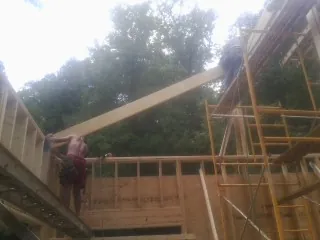 Carpenter raising a rafter beam on a new second story frame in Essex